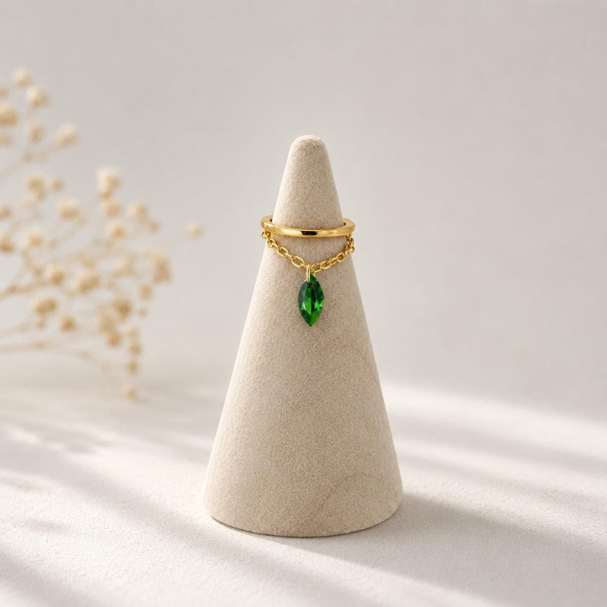 A gold ear cuff with a dangling green marquise crystal resting on a beige cone display stand.
